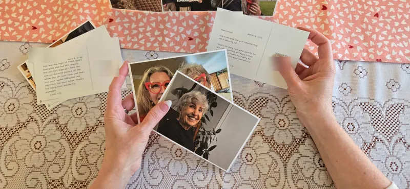 Two hands holding photo postcards, the photo side in one hand and a handwritten message in the other