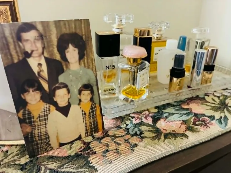 A 1970s family portrait postcard on a nightstand beside a tray of perfume bottles